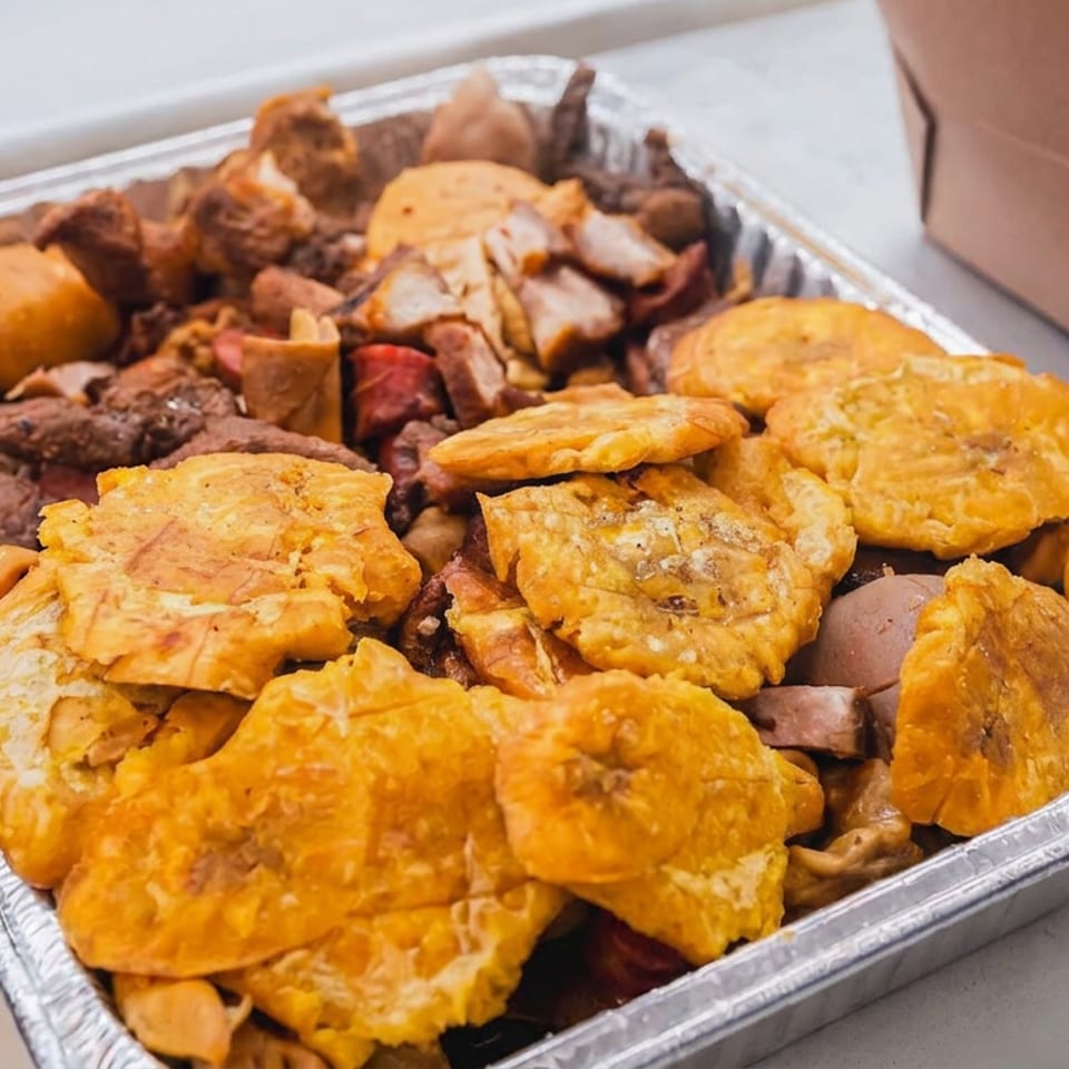 Aluminum catering tray filled with fried plantains, meat, pasta, and assorted savory dishes.